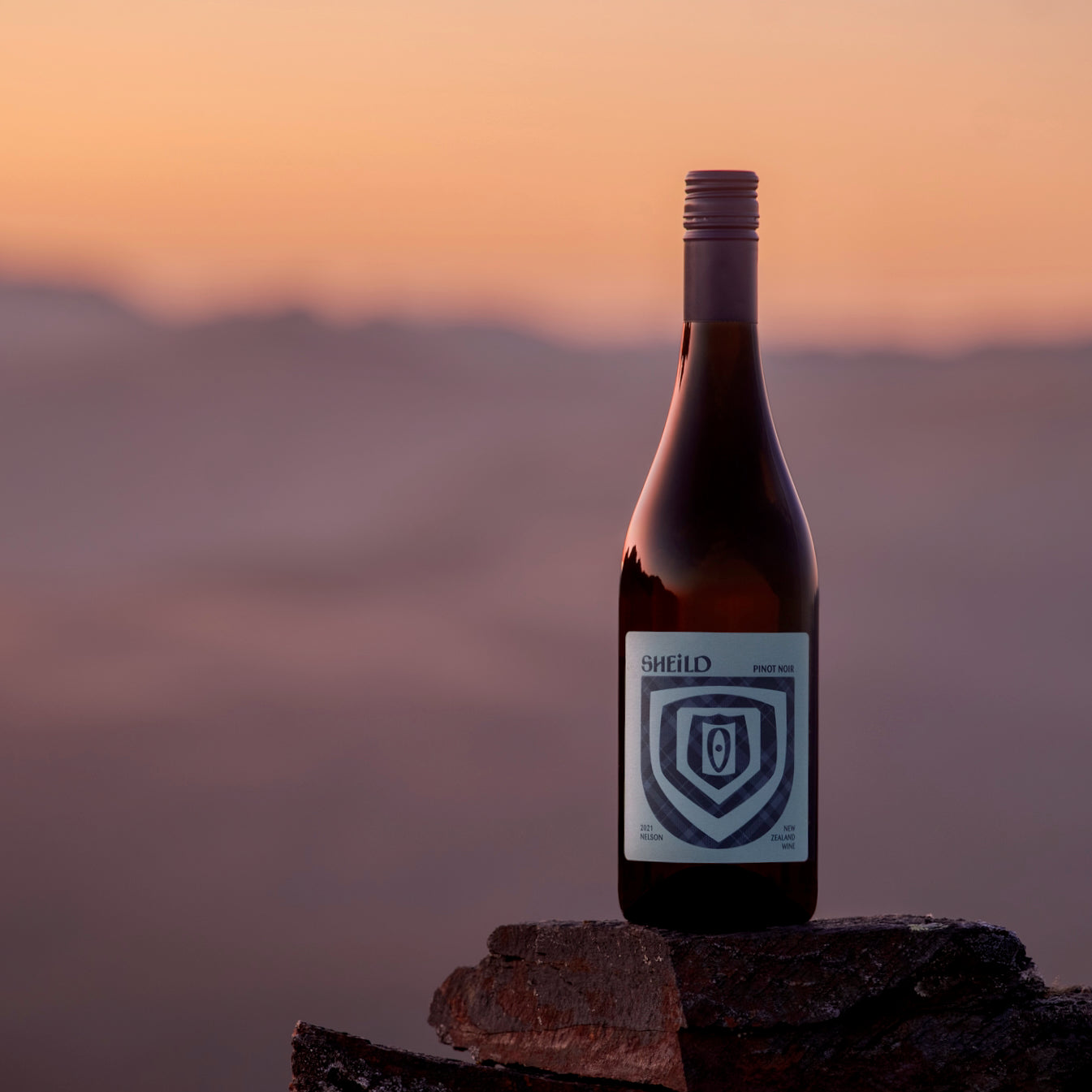 SHEiLD's Pinot Noir wine placed on a rock at the top of a mountain at sunset.